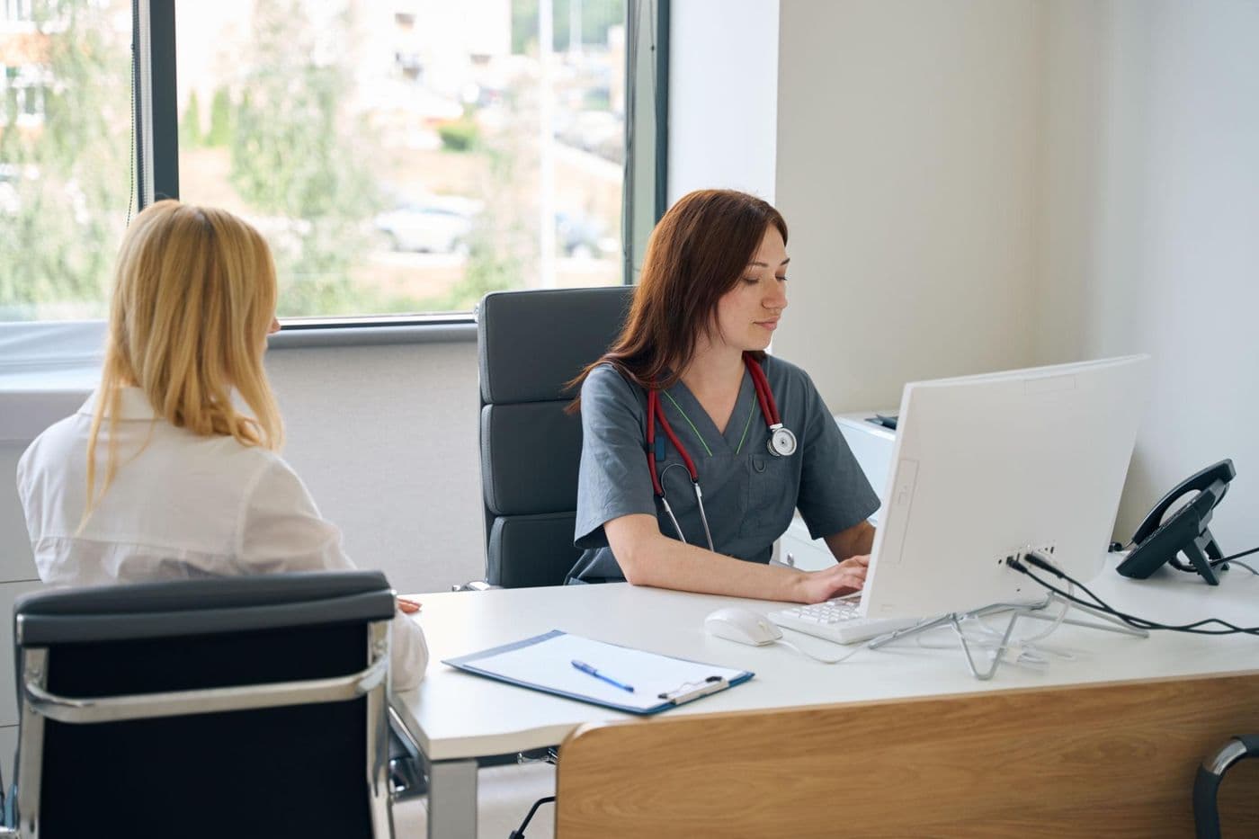 Médica atendendo uma paciente em consultório, registrando a consulta no computador